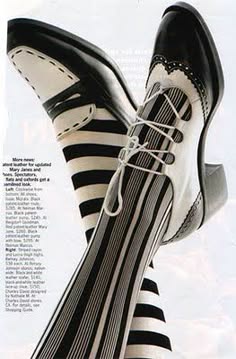 a close up of a model's leg wearing black and white striped stockings and black and white shoes.  the model is wearing high heeled shoes with white trim.  the image is cropped at the knee.