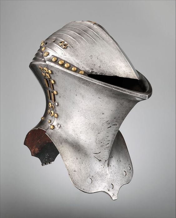 a closeup view of a 16thcentury german helmet made of steel. the helmet features a distinctive design with a high, pointed crown and a series of vertical ribs. it is adorned with gold rivets and has a slightly aged, metallic gray finish. the background is a neutral gray, highlighting the intricate details of the helmet.