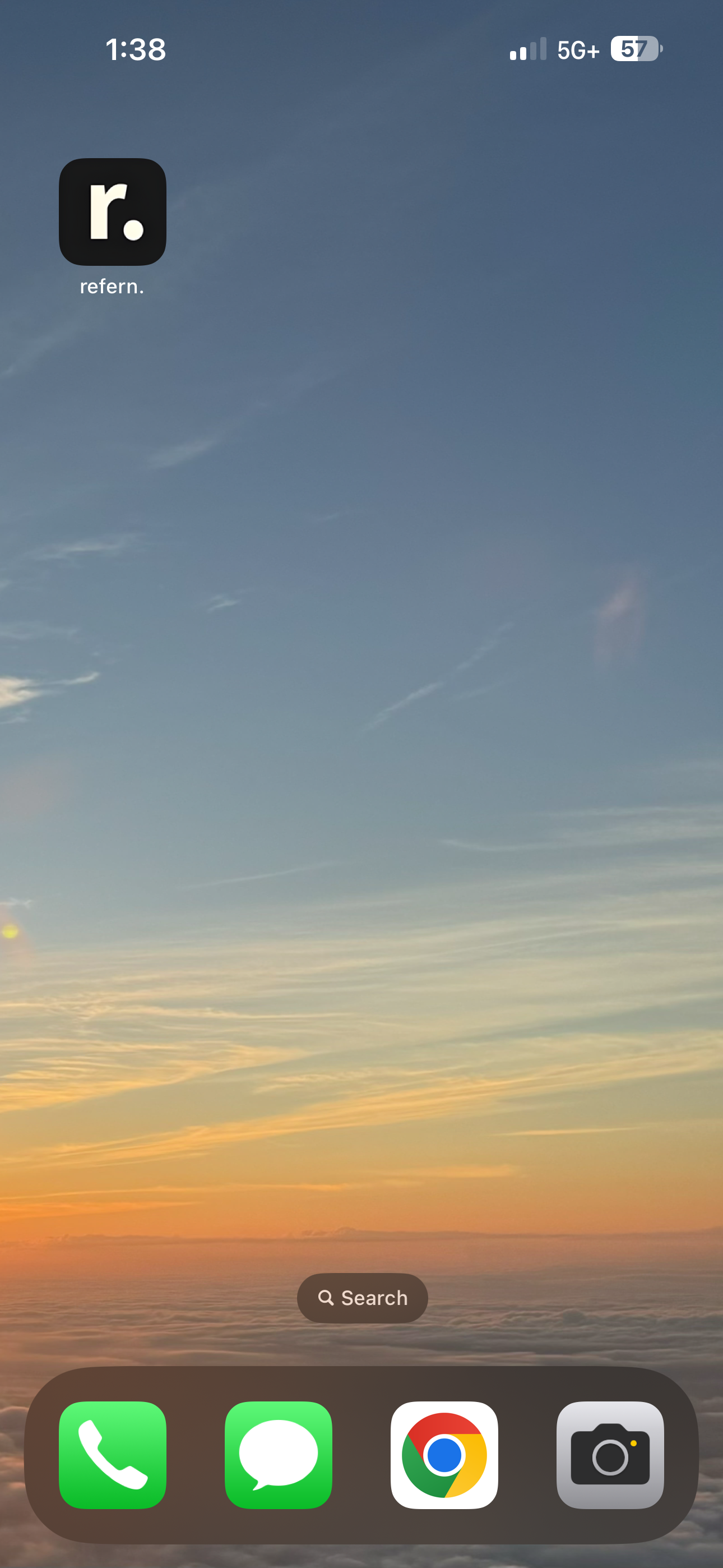 a closeup of an iphone screen with a refern app icon in the top left corner and a home screen view below.  the phone has four icons in the dock  phone, messages, chrome, and camera.  the background is a sunset sky with clouds.