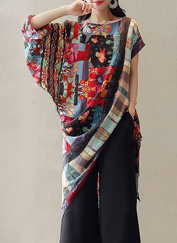 a woman wearing a colorful floral print tunic over black wide leg pants. the tunic has an asymmetrical design and an oversized fit. she is also wearing earrings.