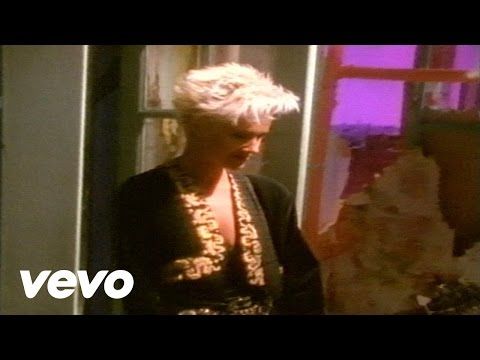 a woman with blond, spiked hair wearing a black jacket with decorative trim stands against an abstract background. the vevo logo is visible in the bottom left corner, suggesting this is a still from a music video. the color palette and styling indicate a possible timeframe of the 1980s.