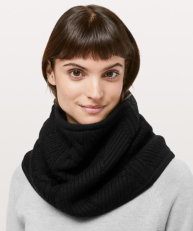 a woman models a black knit neck warmer against a white background.  she has brown hair cut in a bob and is wearing a grey sweater.