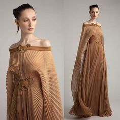 two beautiful women are wearing long, pleated, brown gowns in a studio. they are posing for a photo shoot. the gowns are sophisticated and elegant, with a highfashion aesthetic. the women are both beautiful and glamorous, and their outfits make them look incredibly chic. the dresses are designed in a way that highlights their feminine figures. the photos are likely part of a fashion campaign or look book.