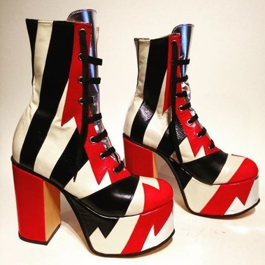 a pair of eyecatching platform boots with a bold design. the boots feature a black and white striped pattern on the upper part of the boot, a red accent on the front with zigzag details, a high block heel in red, and a chunky platform sole also with red and white zigzag. they have a laceup closure with black laces. the boots look fashionable and unconventional.
