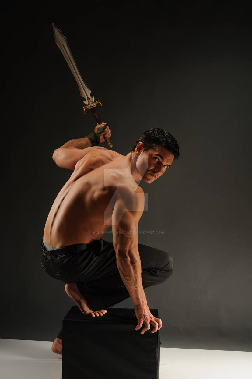 a muscular man wearing black pants is posing dramatically with a sword. he is crouching on a black box, looking over his shoulder, with a determined expression on his face.  the lighting is dark and dramatic, creating a sense of power and intensity.  the image suggests a scene of action or fantasy, with the man perhaps about to charge into battle.