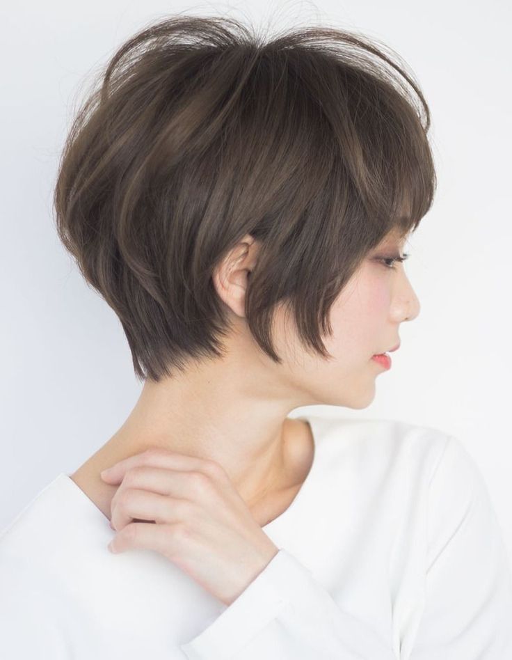 a young woman with short brown hair is wearing a white shirt. she is looking away from the camera and has her hand on her neck. the photo is taken from the side.