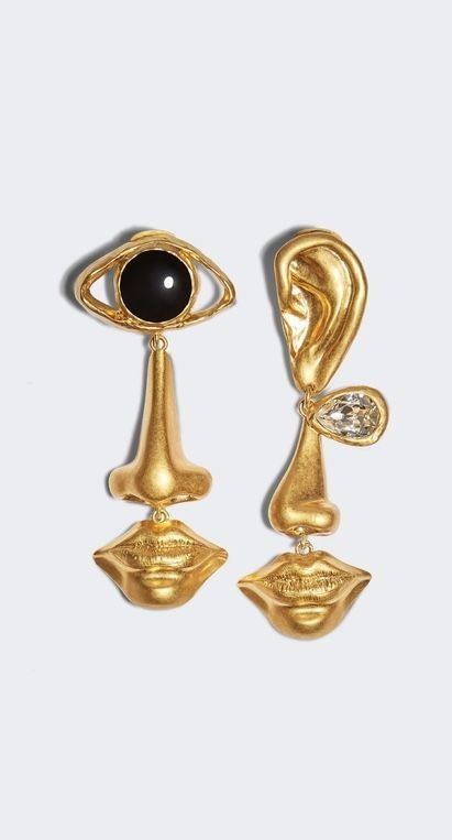a pair of gold earrings with a surreal and abstract design. the earrings feature a gold eye, nose, lips, and ear, each element crafted in a realistic and detailed manner. the earrings are suspended from a delicate chain and are perfect for adding a touch of whimsy and personality to any outfit.