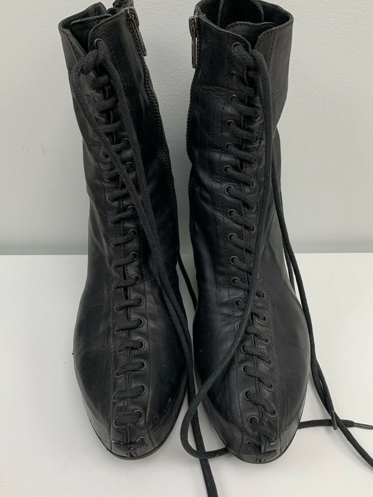 two black laced boots are standing on a white surface. the boots are laced up the front and have zippers on the sides.