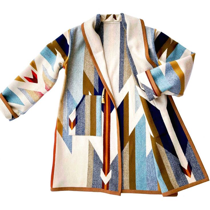 this is a women's coat made of wool with a pattern of geometric shapes. it is white with accents of blue, brown, red, and gold. the coat has a shawl collar.