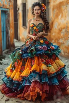 a woman wearing a vibrant, multilayered and multicolored dress stands on a cobblestone street. the dress features intricate floral embroidery and ruffles. the warm, natural light illuminates her and highlights the rich colors of her attire and the surrounding environment.