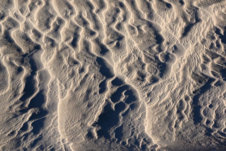 a closeup shot of sand dunes in a desert. the wind has eroded the sand, creating a pattern of ripples and waves. the light and shadow create an abstract pattern on the surface of the sand.