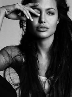 a black and white portrait of a woman with long dark hair. she is looking at the camera with a serious expression on her face. her hair is covering one of her eyes and her lips are slightly parted. she is wearing a black and white outfit and her makeup is very dramatic. the photo is taken in a dark and moody setting. the overall impression is one of elegance, sensuality and mystery.