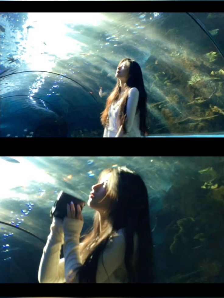 the image is a diptych showing a young asian woman with long brown hair in an underwater tunnel aquarium.  in the top image, she stands looking upwards, seemingly in awe of the surrounding marine life and light. she's wearing a light creamcolored sweater. the bottom image shows her from a slightly lower angle; she is holding a small camera or similar device to her face, still within the aquarium tunnel.  the lighting in both images emphasizes the underwater setting, with sunlight filtering through the water and illuminating the woman and the fish around her. the overall mood is serene and peaceful.