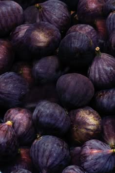 a close up photo of a large pile of ripe purple figs, some of the figs have blemishes and are browning, while others are deep and dark purple. the figs are arranged in a heap, with some overlapping, some in the background, and others in the foreground.