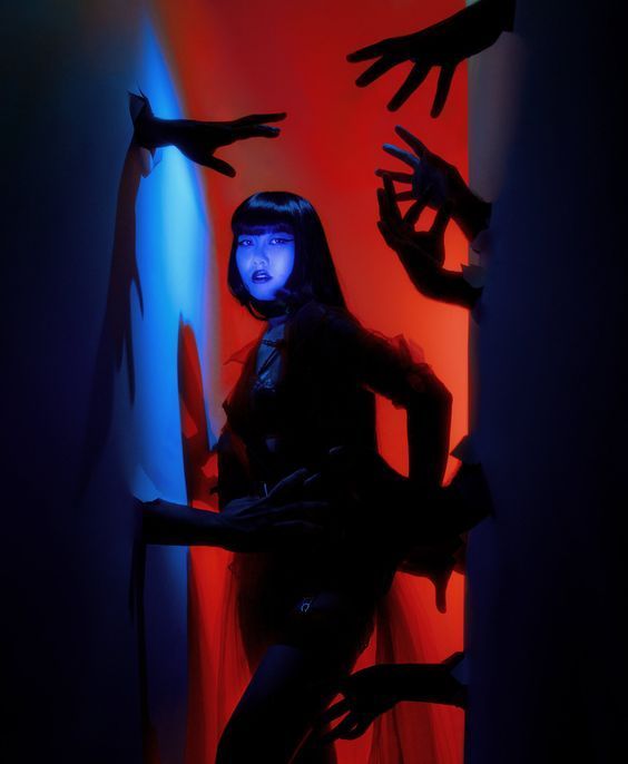 a woman with long dark hair stands in a red lit doorway, surrounded by a shadowy figure.  there are multiple hands reaching out from both sides of the doorway, creating a mysterious and spooky ambiance.