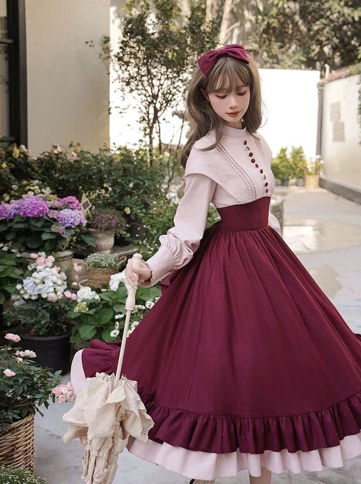 a young woman in a vintagestyle lolita dress stands gracefully in a garden setting. she holds a lace parasol, and her outfit features a burgundy skirt and a pink blouse with delicate buttons. the image evokes a sense of romanticism and elegance, highlighted by the soft, natural lighting.