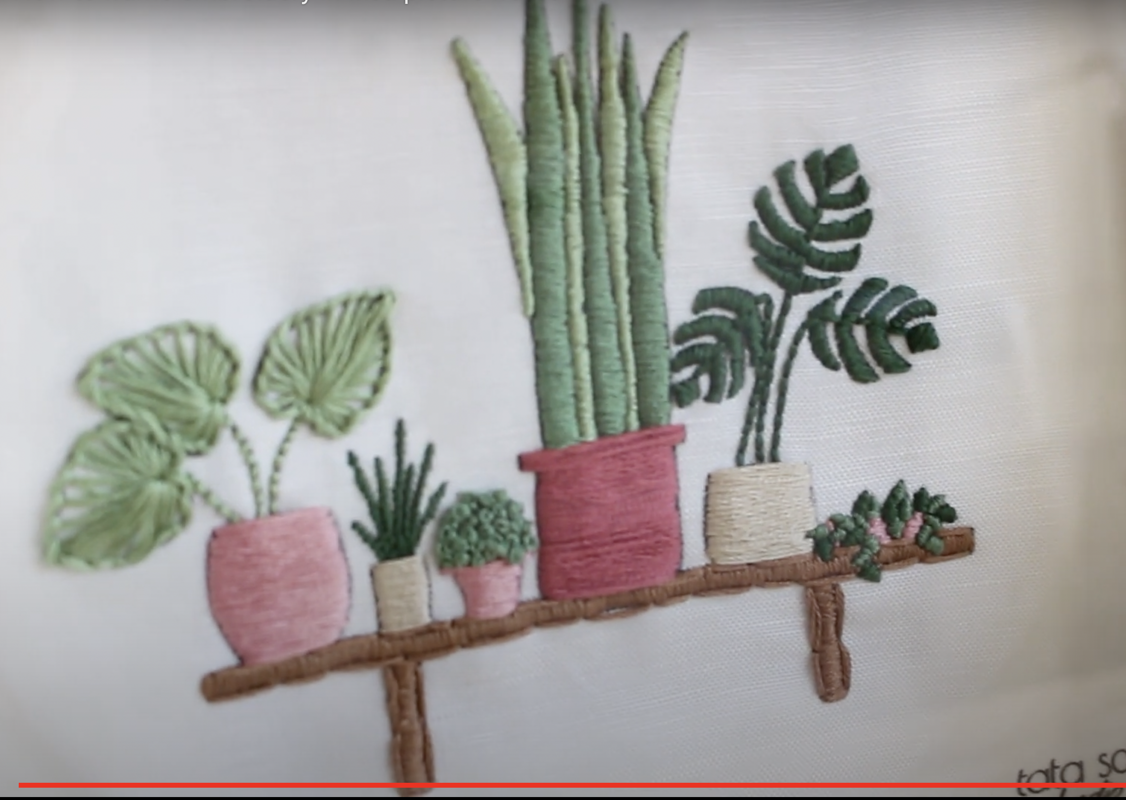 the image shows an embroidery art piece featuring a variety of potted plants arranged on a wooden shelf. the plants include a snake plant, a monstera deliciosa, and other smaller leafy greens. the shelf and pots are also embroidered, creating a cohesive and charming design. the artwork is done on a white fabric background, highlighting the vibrant green and earthy tones of the embroidery.