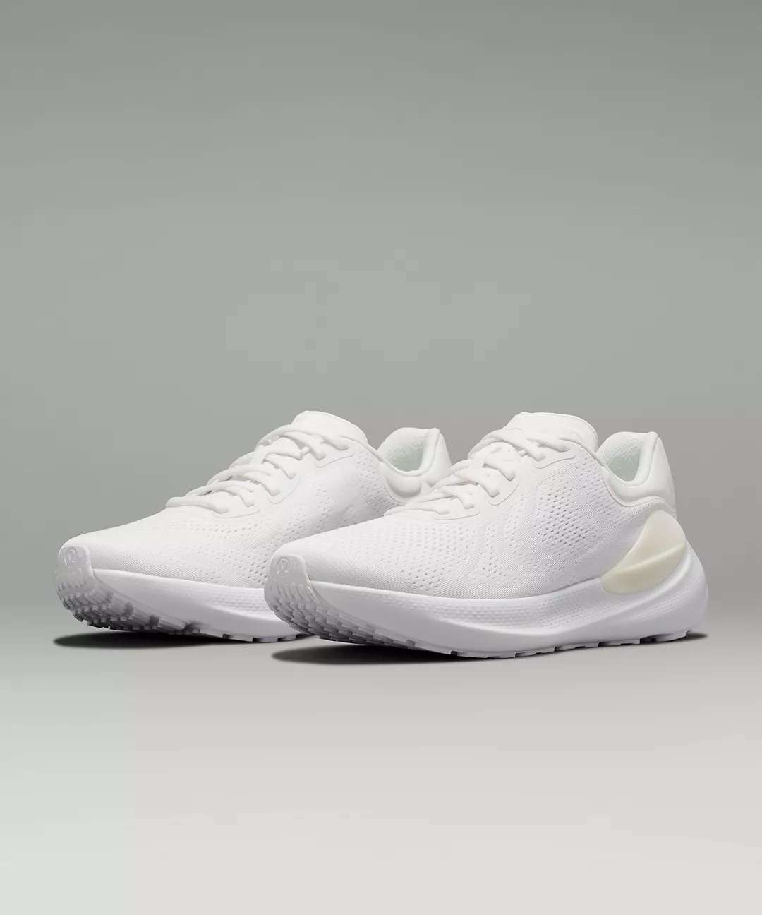 a closeup studio shot of a pair of white sneakers.  the shoes are clean and minimalist in design, with a lightcolored sole and a breathable upper. they appear to be running shoes or athletic trainers, suitable for exercise or casual wear. the background is a simple, neutral gray, allowing the shoes to be the main focus of the image.