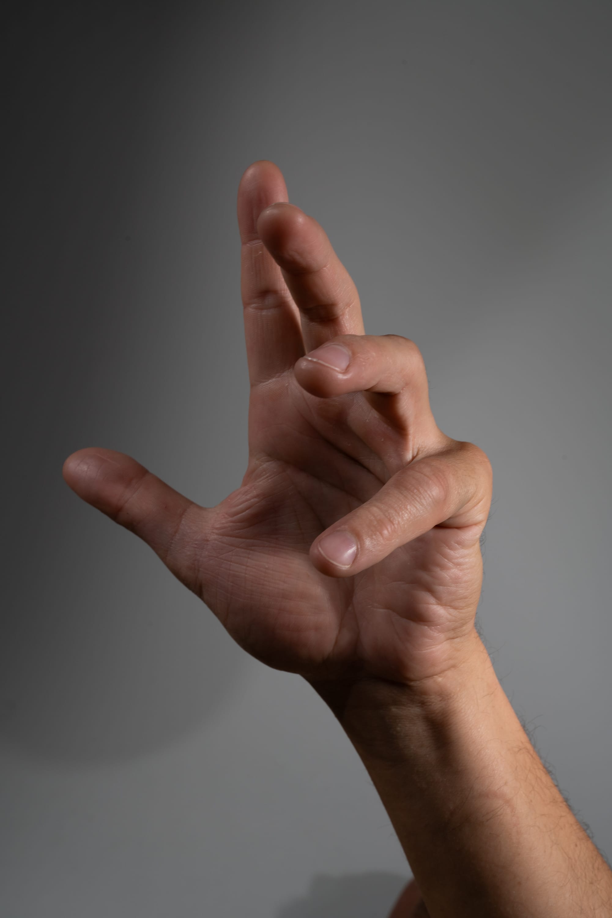 a hand is extended upwards against a gray background. the hand is making a gesture with the index and middle fingers extended and the other fingers curled in. the image is lit with studio lighting and taken from a worm's eye view.