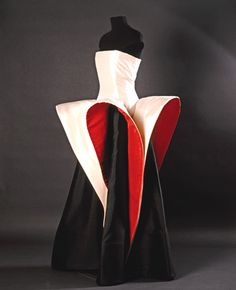 a closeup shot of a fashion model wearing a dramatic avantgarde dress. the dress is a white and red geometric design with a black skirt. the dress is very abstract and has a lot of volume. the model is standing on a black background. the dress is very elegant and sophisticated, and the model's pose is very dramatic.