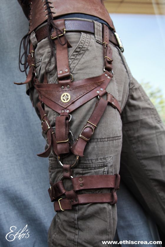 the image showcases a closeup of an elaborate, handcrafted steampunkinspired leg harness worn over khaki cargo pants. the harness, made of rich brown leather, features intricate straps, buckles, and metal accents. a central triangular piece adorned with a gearlike emblem adds a touch of industrial flair.  the soft lighting emphasizes the texture of the leather and the craftsmanship of the piece.