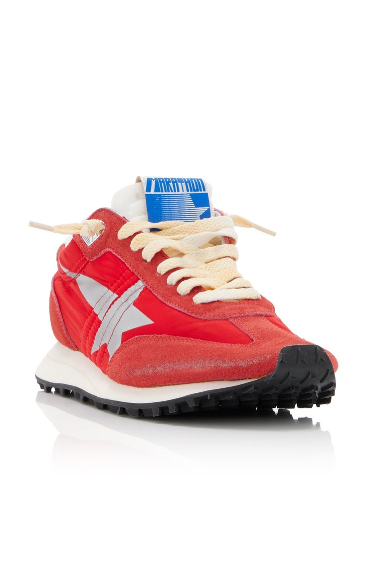 a closeup shot of a single golden goose red suede sneaker. the shoe is predominantly red with a silver star detail on the side and a blue "marathon" label on the tongue. the laces are offwhite, and the sole is offwhite with black treads. the background is a plain white, creating a clean backdrop that focuses attention on the shoe. the image showcases the shoe's details and texture clearly.