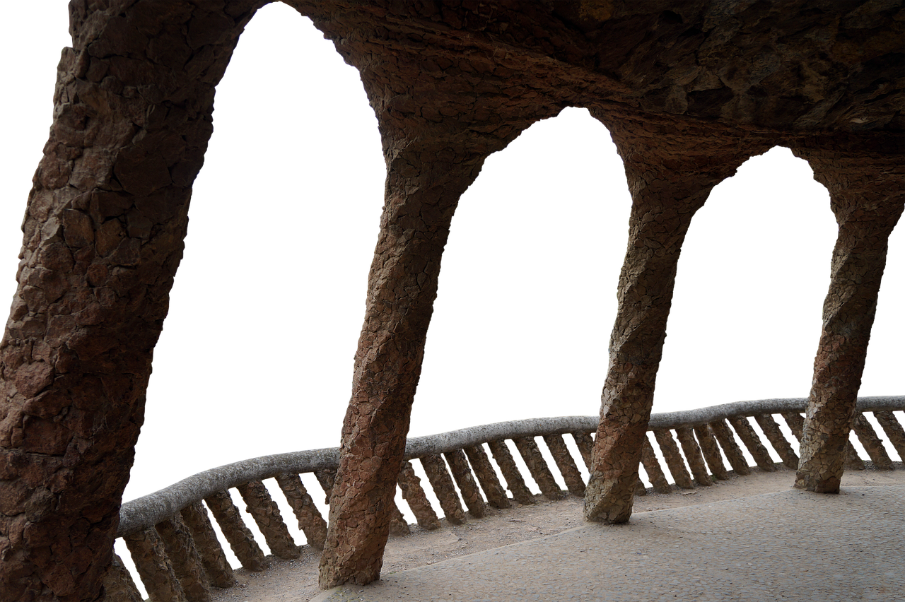 this image shows a section of the park güell architecture in barcelona. the foreground features a stone walkway with a concrete railing. arches are formed by stone columns, each of them textured with individual stones. a deep black background is visible through the arches.