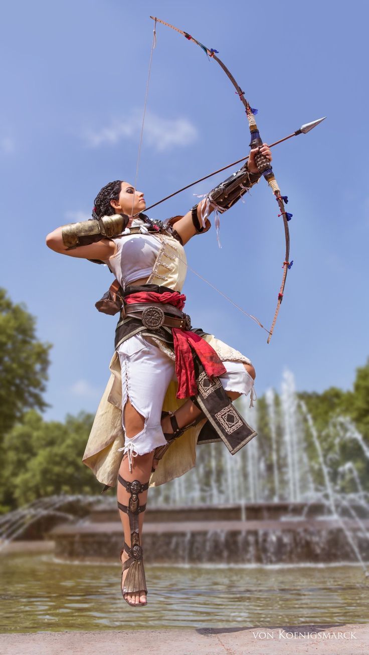 a woman dressed in a white and gold costume is captured midair, gracefully launching an arrow from her bow.  the archer, potentially cosplaying a character, exudes strength and focus against a backdrop of a park fountain on a sunny day. the low camera angle accentuates the dynamism of the pose.