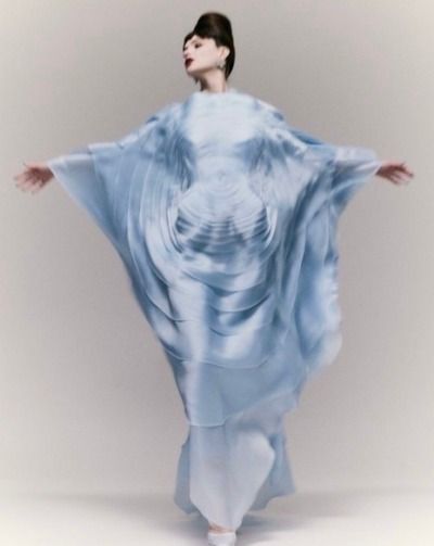 a woman in a flowing, blue dress poses elegantly for a studio portrait. the dress has a beautiful, layered design and accentuates the woman's figure. the lighting is soft and flattering, highlighting the woman's beauty.