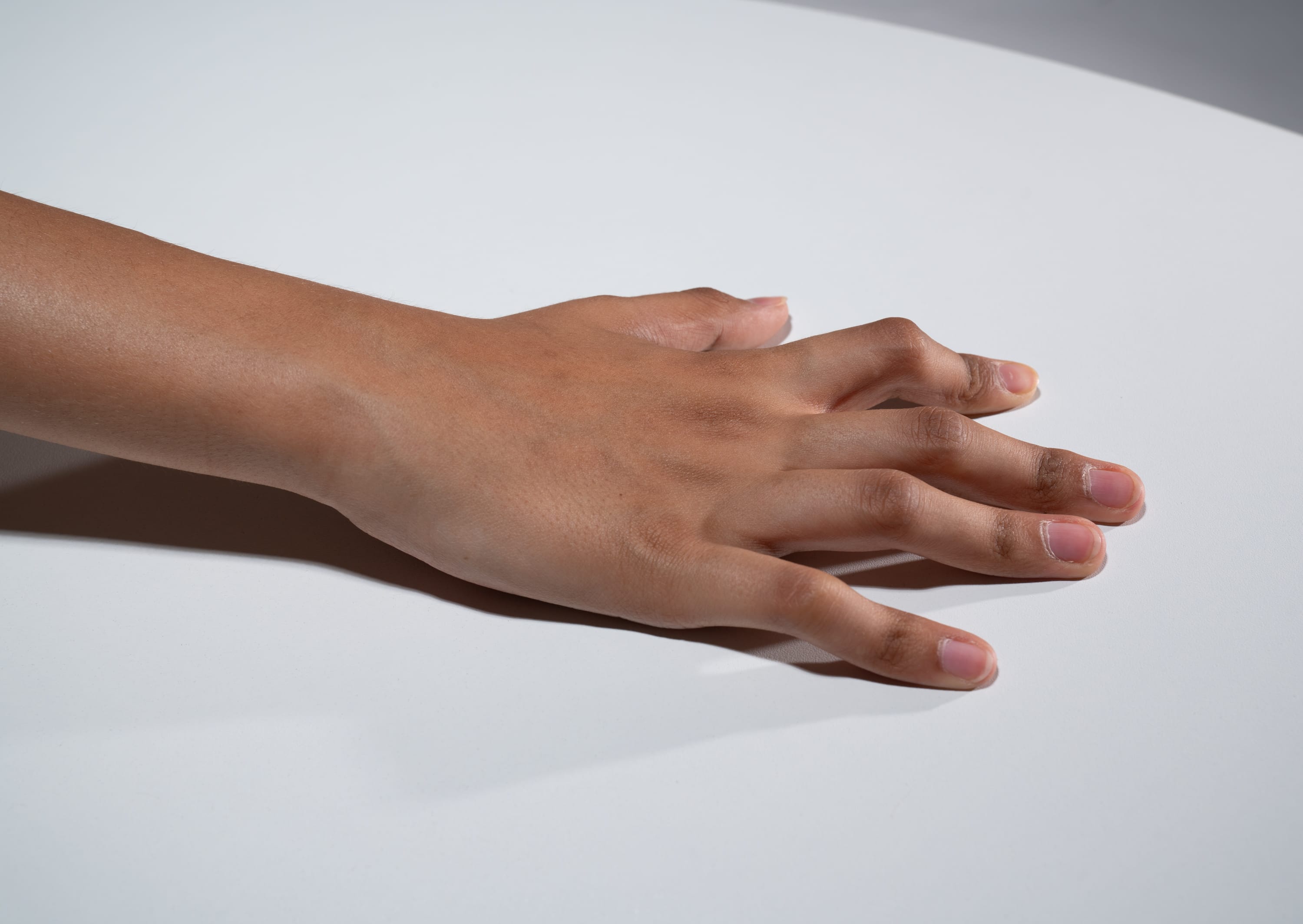 an image of a person's hand with brown skin lying on a white table. the image is taken from a top view perspective and features soft lighting, highlighting the details of the hand and the texture of the skin.