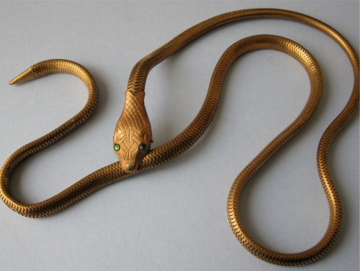 a gold snake necklace with green eyes is shown on a white surface.