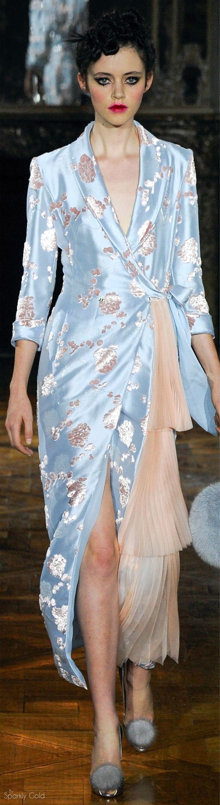 a woman is posed in a beautiful, flowy blue and pink floral dress, with her hair slicked back, and wearing elegant, pointed heels. the woman is in a studio setting and she is looking directly at the camera.  her pose is elegant and graceful.  the dress has a wraparound style and a soft flowing train.  her shoes are a delicate pink, with a pointed toe and a high heel.  the overall effect is one of elegance and sophistication.