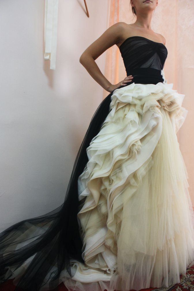 a woman in a white and black dress stands in front of a white wall. the dress has black tulle on the bottom half and white tulle on the top half. it has a ruched skirt and a black bodice. the woman is looking off to the side.