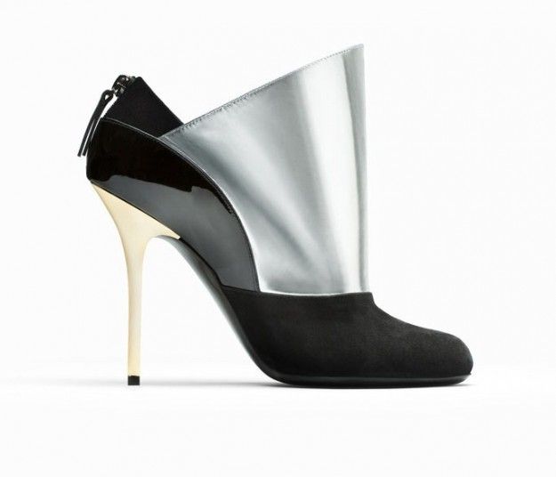 a side view of a stylish highheeled ankle boot with a black suede toe, a black patent leather heel, a silver leather upper, and a gold stiletto heel. the boot has a zipper closure at the back.