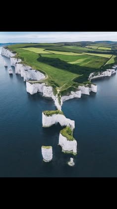 an aerial shot of a coastline, a beautiful landscape with a series of white cliffs with green grassy land on top and water all around.