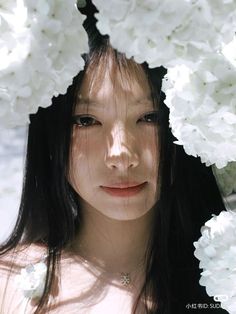 a young woman with long dark hair is looking directly at the camera. she is wearing a delicate silver necklace and is surrounded by white flowers, creating a soft and romantic atmosphere. the natural lighting illuminates her face beautifully, highlighting her features.