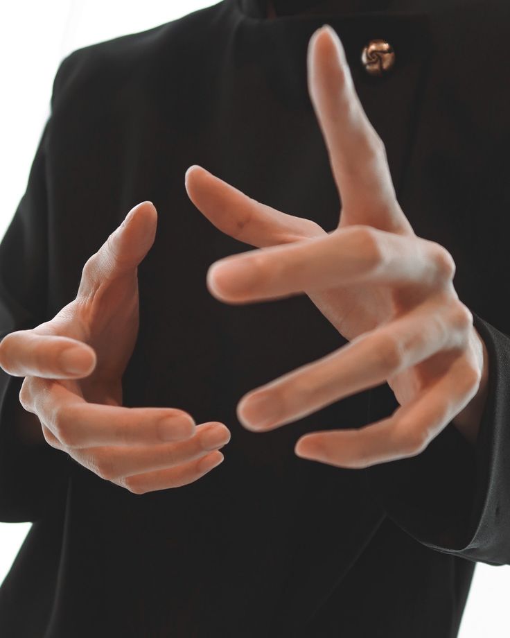 a man in a black blazer is wearing an elegant jacket and is posing with his hands extended in front of him. the hands are visible in the front of the image, and the rest of the blazer is shown in the background. he is giving a serious and mysterious expression.