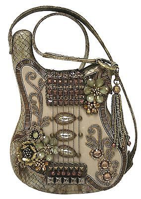 a decorative handbag shaped like a guitar is shown. the bag has a beige base and is heavily embellished with beads, stones, and floral accents. it features a shoulder strap, a decorative tassel, and elements resembling guitar components like pickups and a bridge. the design has a vintage or handcrafted appearance.