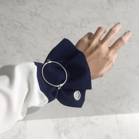 a closeup image shows a person's arm and hand wearing a white and navy blue shirt with a silver bracelet. the bracelet has a silver ring as a decorative element. the hand is outstretched.