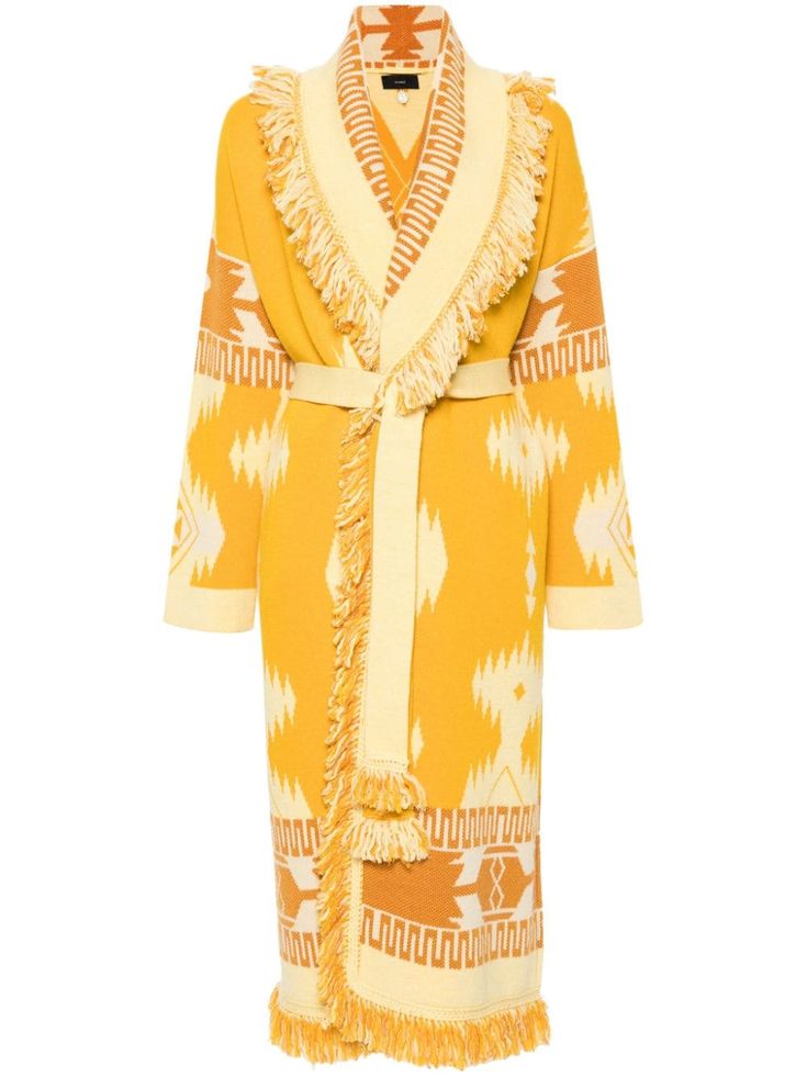 this is a yellow knit cardigan featuring fringe detailing and a geometric pattern. it is long and fits loosely, making it a perfect warm and cozy piece of clothing for fall or winter.