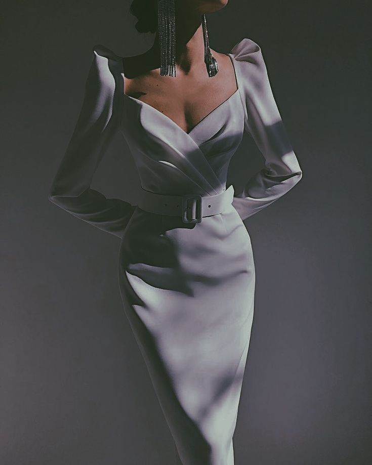 the image shows a woman wearing a stylish, elegant white dress. the dress has long sleeves with puff shoulders, a fitted bodice, and a midilength skirt. it features a vneckline and a wide belt around the waist. the woman is wearing long dangling earrings, and her pose and attire convey sophistication and glamour. the background is a simple, neutral grey, making the dress and model the focal points of the image. the lighting is soft and dramatic, enhancing the overall mood and aesthetics.
