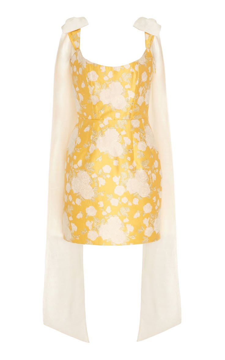 a yellow and white floral cocktail dress with ribbon straps is displayed on a white background. the dress has a yellow base with a white floral pattern overlaying it. the dress has a formfitting bodice and a short skirt. two long, white ribbons are attached to the straps and hang down the front of the dress on both sides.