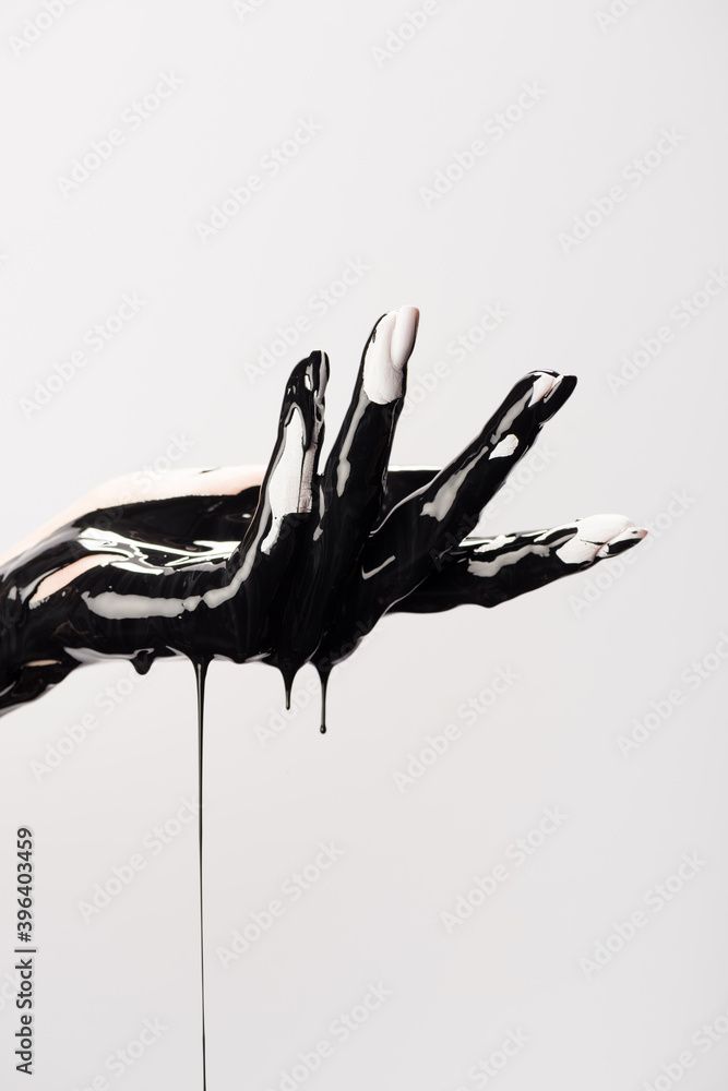 a closeup image of a hand painted in black paint dripping against a white background. the hand is in a relaxed, open position, with the fingers spread apart. the paint is thick and glossy, and it is dripping down the hand and onto the background. the image is artistic and abstract, and it is likely to be used as a part of a creative project.