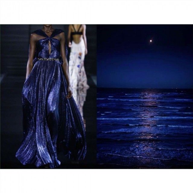 the image shows a split composition. on the left, a darkskinned model is wearing a shimmering, deep blue, pleated dress on what appears to be a runway. another model is walking behind her in a white gown. on the right, there is a night scene of a dark ocean with waves and a moon reflecting on the water. the color palette aligns between the dress and the ocean, creating a visual connection.