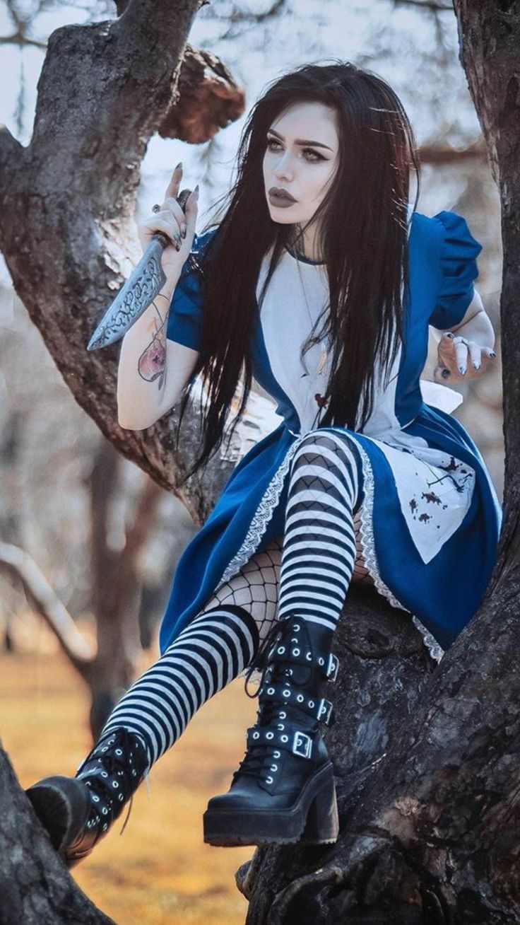a dark and dramatic cosplay portrayal of alice from alice in wonderland. the model, with long black hair, is dressed in a blue and white dress reminiscent of alice's attire, but with a darker, more gothic twist. she is sitting on a tree trunk in a forest setting, holding a knife. her stockings are striped, and her boots are chunky and black. the overall mood is mysterious and edgy, a blend of whimsical fantasy and macabre gothic elements. the image is professionally shot, with attention to detail in both the costume and the setting.