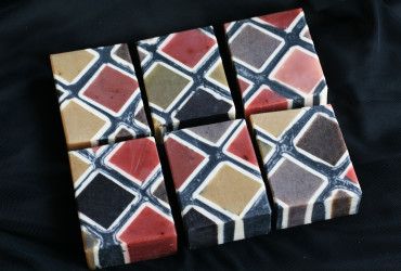 a collection of six geometrically patterned bars of soap, displayed in a diamond formation on a dark background. the colors are bold and vibrant, creating a striking contrast. the bars are crafted with care and attention to detail, making them both beautiful and functional.