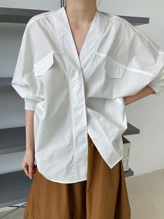 a woman wearing a white oversized shirt with a brown skirt is standing in front of a white background. she has her hair pulled back and is looking at the camera. the shirt is long and has a button down front. the sleeves are long and are cuffed at the wrists. the skirt is a brown aline skirt that falls to just above her knees. she looks casual and comfortable in her outfit.