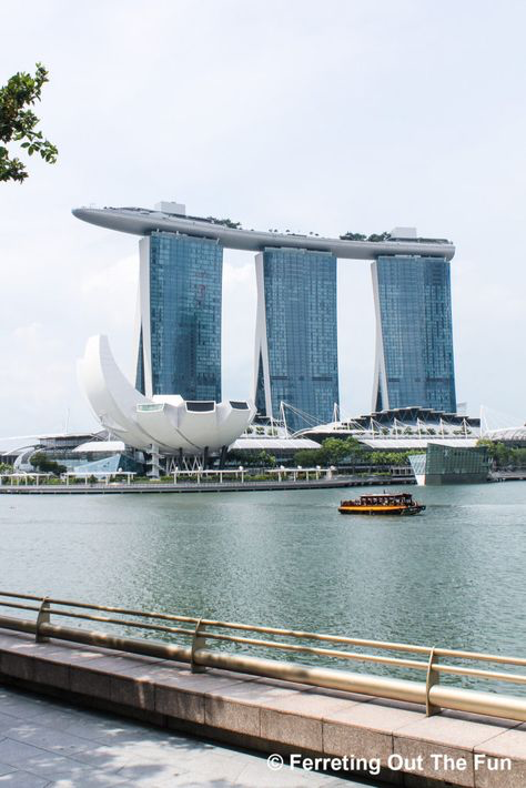 a photo of the marina bay sands hotel in singapore. the three towers of the hotel are visible, along with the iconic boatshaped structure on top. a small boat is on the water in front of the hotel. the photo is taken from a waterfront viewpoint.