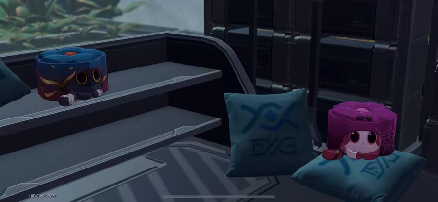 a closeup shot of an anime character sitting on a pillow inside a futuristic spaceship. the character is wearing a red and purple hat and has big eyes. the background features a blue pillow with a symbol on it, along with other seats. the scene is filled with bright, colorful hues, creating a whimsical and vibrant atmosphere. the image is suggestive of an animated game or film.