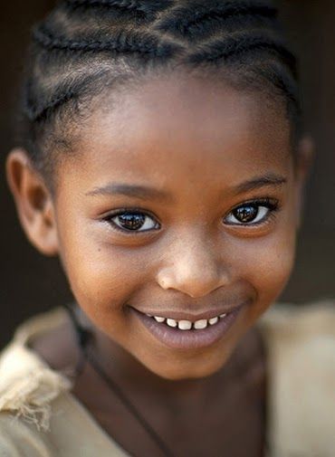 a closeup portrait of a young girl with dark skin and a bright smile. she has braids in her hair and her eyes are wide and expressive.